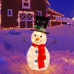 A wireframe snowman with pure white lights inside with white fabric for the skin, a red long tied scarf, and a top hat with mistletoe and berries on it. This decoration is in a snowy field with Farmhouse Christmas decor in the background that is lined with warm white Christmas lights.