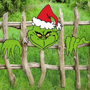 A wooden form of the grinch appearing to look through a rugged wooden fence in a field