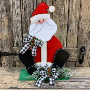 A solid wood Santa with plaid bows on his shoulder and at his feet