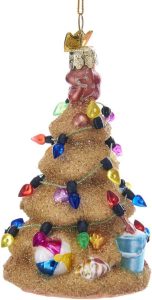 A Christmas tree decoration in the shape of a Christmas tree made from sandstone with lights around it and beach items at the base